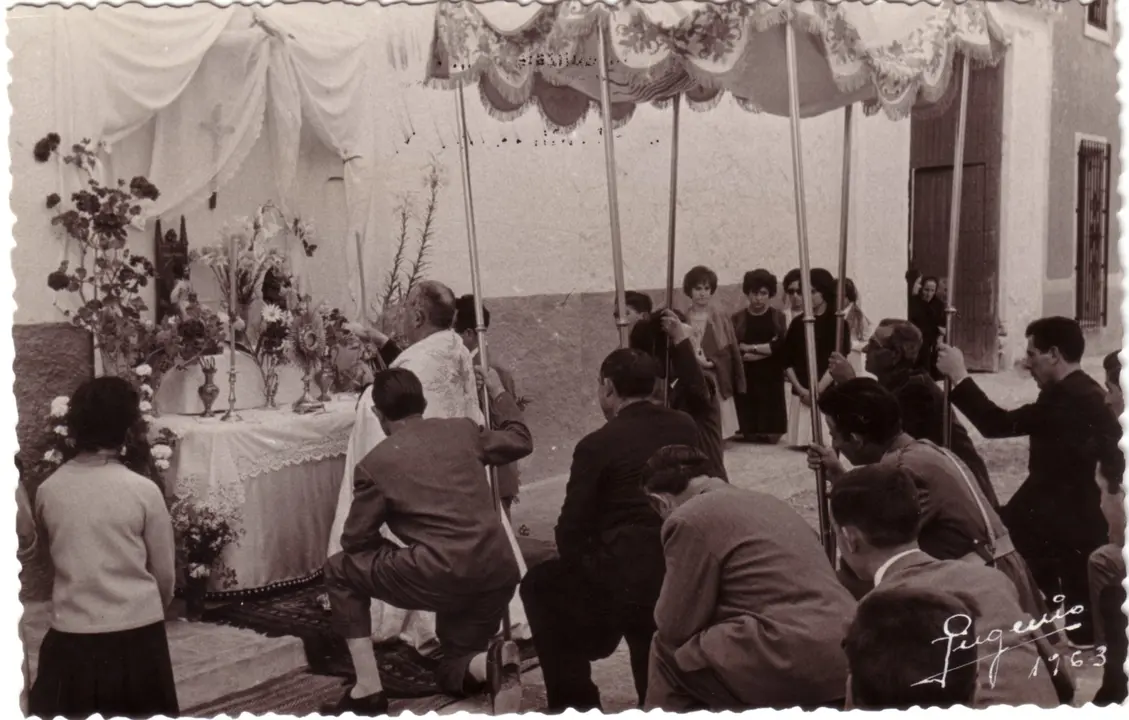 Sacerdote y feligreses orando de rodillas ante un altar en la calle durante la celebración del Corpus Christi de Barrax (Albacete). 1963. Fondo Los Legados de la Tierra. Archivo de la Imagen de Castilla-La Mancha.
