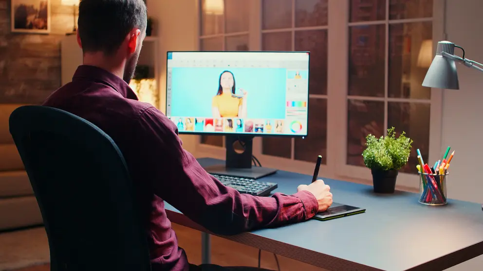 Male photographer editing photos in office at night time using graphic tablet.